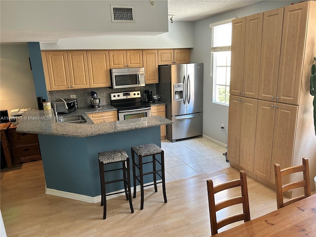 kitchen featuring a breakfast bar, sink, decorative backsplash, kitchen peninsula, and stainless steel appliances