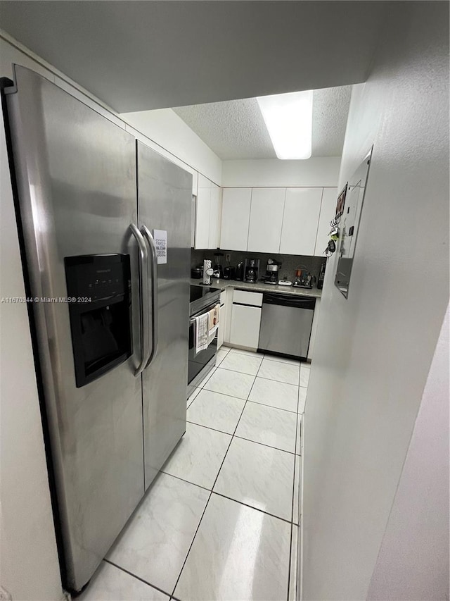 kitchen featuring appliances with stainless steel finishes, backsplash, light tile patterned floors, and white cabinetry