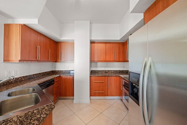 kitchen featuring appliances with stainless steel finishes, dark stone countertops, light tile patterned flooring, and sink