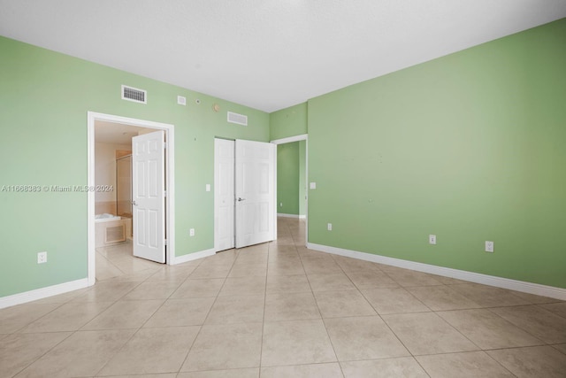 unfurnished bedroom with connected bathroom and light tile patterned floors