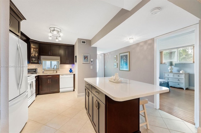 kitchen with sink, white appliances, a kitchen island, dark brown cabinets, and light wood-type flooring