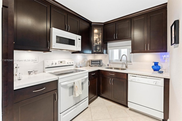 kitchen featuring dark brown cabinetry, backsplash, sink, and white appliances