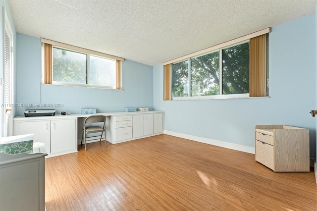 unfurnished office with a textured ceiling, built in desk, light hardwood / wood-style floors, and a healthy amount of sunlight