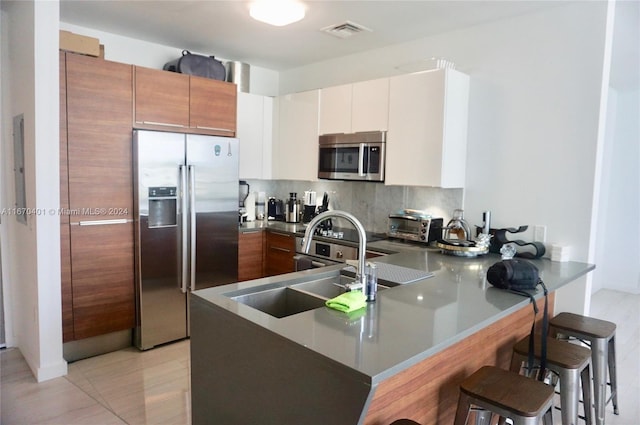 kitchen with appliances with stainless steel finishes, white cabinets, backsplash, kitchen peninsula, and a breakfast bar area