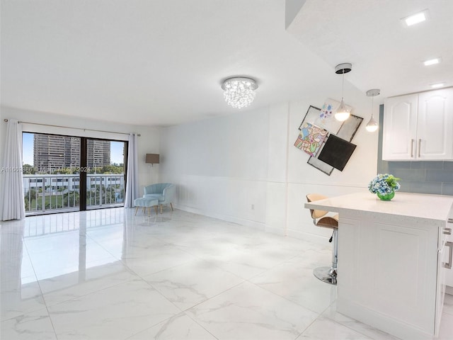 interior space featuring a notable chandelier, white cabinets, a kitchen bar, hanging light fixtures, and backsplash