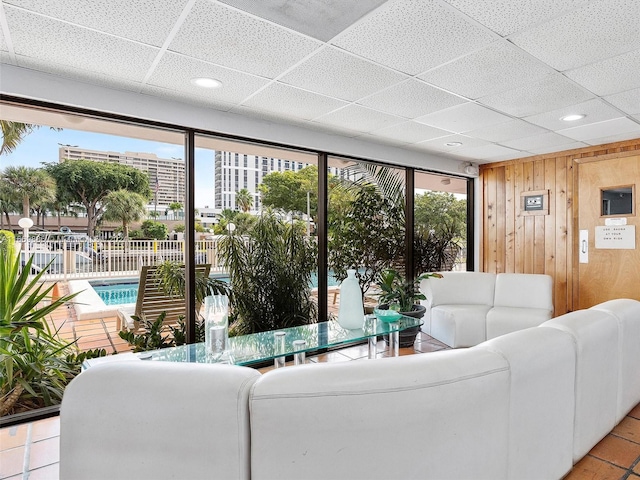 living room with wooden walls, a drop ceiling, light tile patterned flooring, and a wealth of natural light