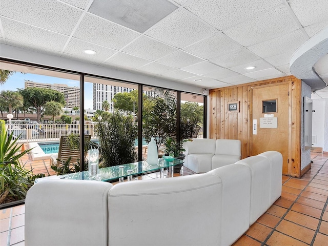 tiled living room featuring a paneled ceiling, wood walls, and a wealth of natural light