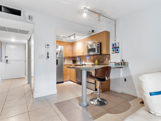 kitchen with a kitchen breakfast bar, decorative backsplash, light tile patterned flooring, kitchen peninsula, and stainless steel appliances