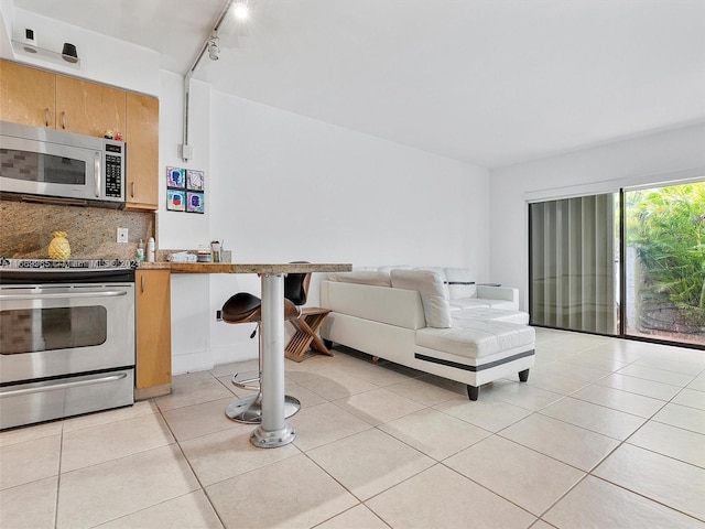 kitchen featuring a kitchen breakfast bar, stainless steel appliances, light tile patterned floors, and rail lighting