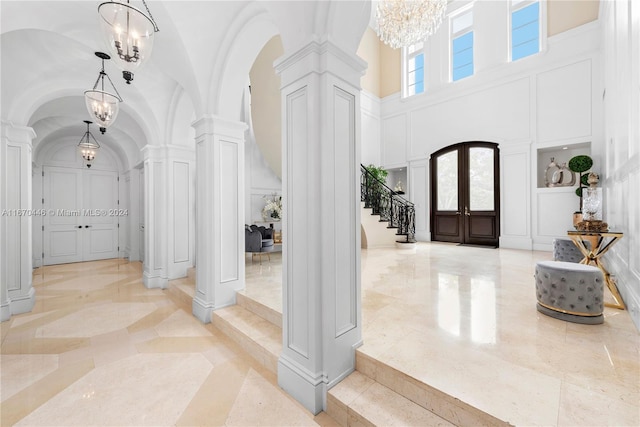 entrance foyer with french doors, a towering ceiling, ornate columns, and a chandelier