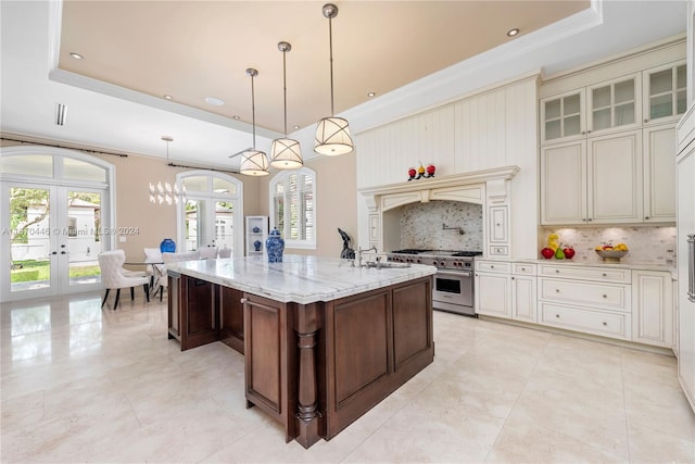 kitchen featuring cream cabinetry, light stone counters, tasteful backsplash, french doors, and a center island with sink