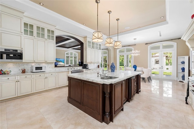 kitchen featuring a healthy amount of sunlight, a center island with sink, french doors, and tasteful backsplash