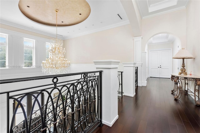 hallway with ornamental molding, a tray ceiling, an inviting chandelier, and dark wood-type flooring