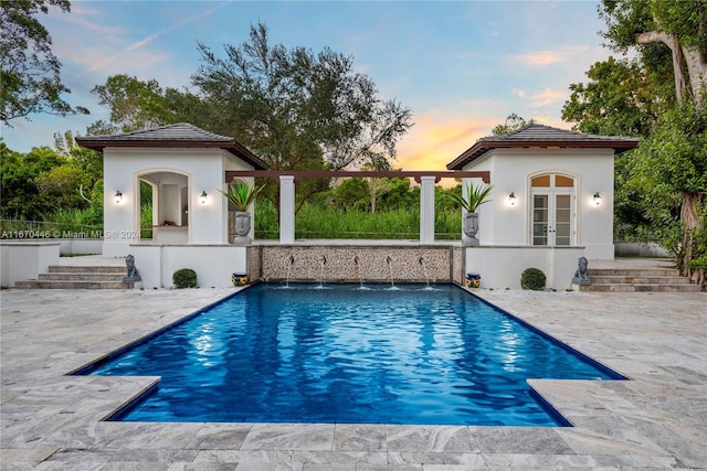 pool at dusk featuring pool water feature, a patio area, and an outbuilding