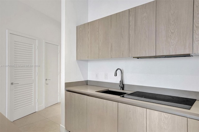 kitchen with black electric cooktop, light brown cabinets, light tile patterned floors, and sink