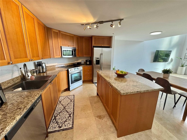 kitchen featuring a kitchen island, light stone countertops, stainless steel appliances, track lighting, and sink