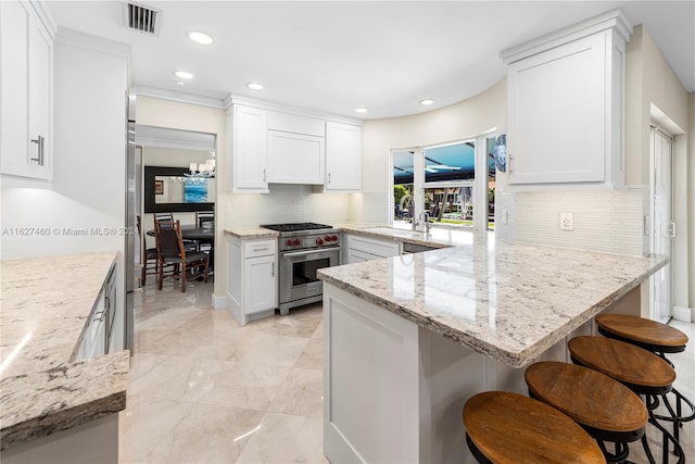 kitchen with tasteful backsplash, designer range, a breakfast bar, sink, and white cabinetry