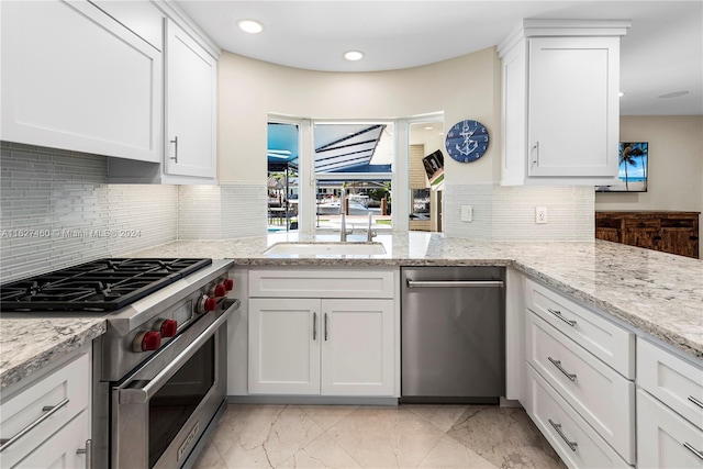 kitchen with white cabinets, light stone counters, premium range, and sink