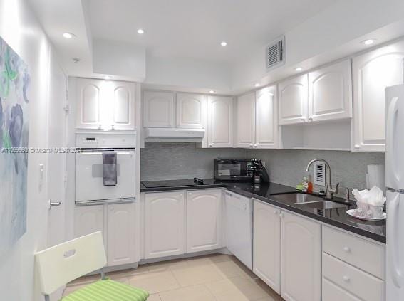 kitchen with white appliances, white cabinetry, sink, and light tile patterned flooring