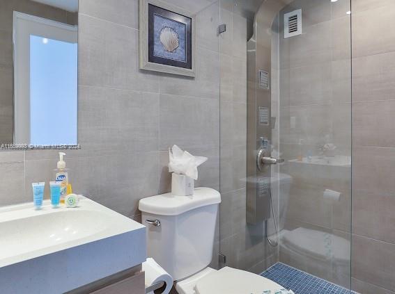 bathroom featuring tile walls, tiled shower, vanity, and toilet