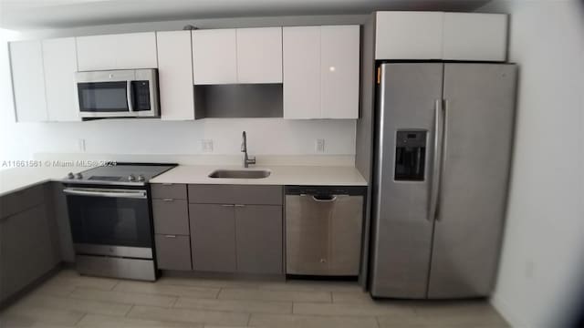 kitchen featuring gray cabinetry, stainless steel appliances, white cabinets, and sink