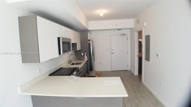 kitchen featuring appliances with stainless steel finishes, kitchen peninsula, white cabinetry, and light hardwood / wood-style flooring