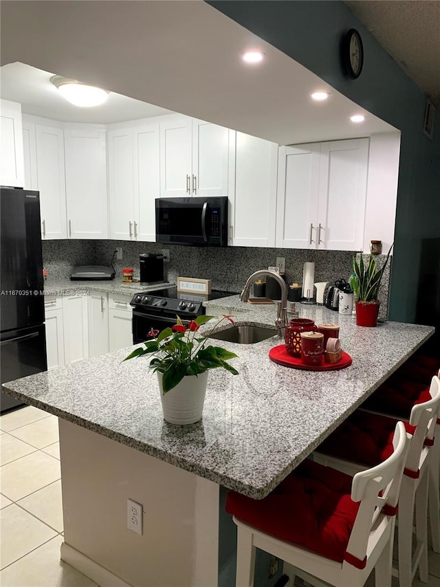 kitchen with range with electric stovetop, white cabinetry, black fridge, and kitchen peninsula