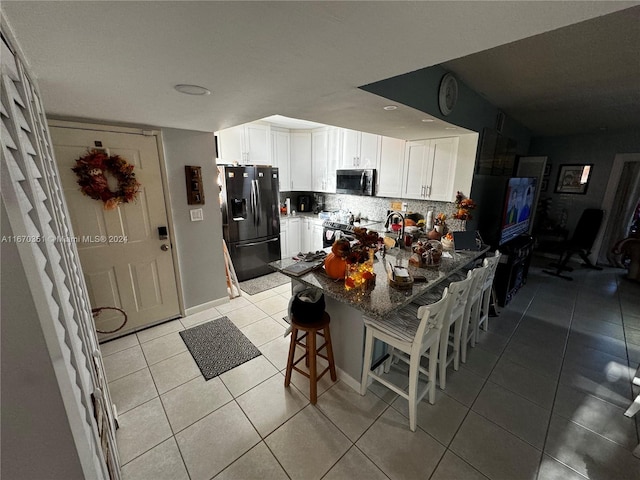 kitchen featuring stainless steel appliances, white cabinetry, a breakfast bar, light tile patterned floors, and decorative backsplash