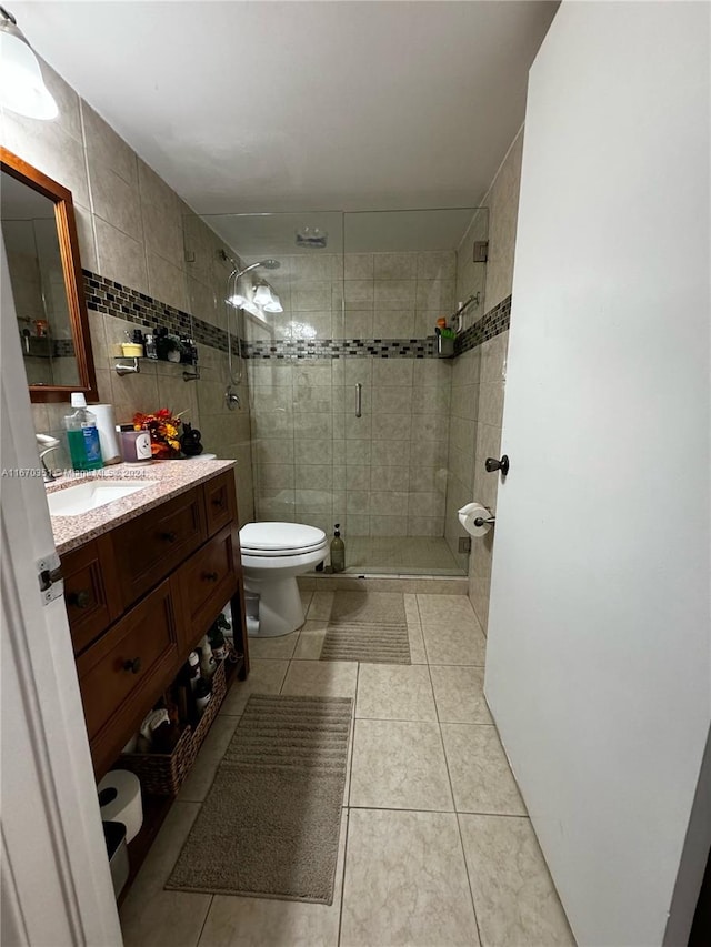 bathroom with a shower with door, tile patterned flooring, vanity, toilet, and tile walls