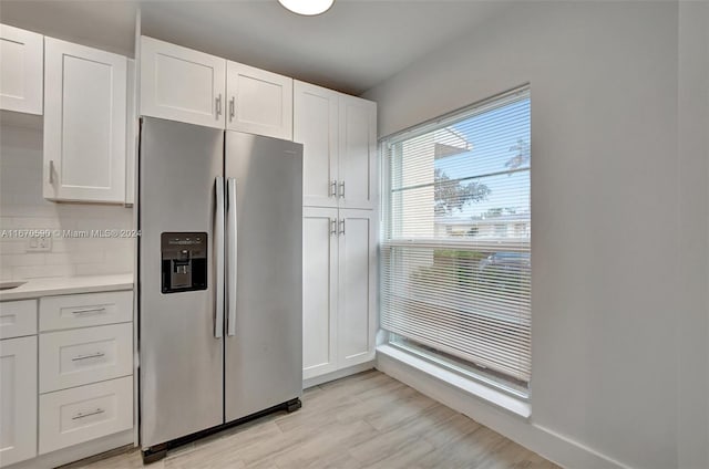 kitchen featuring light wood-type flooring, backsplash, stainless steel fridge with ice dispenser, and white cabinets