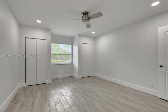 unfurnished bedroom featuring ceiling fan, multiple closets, and light wood-type flooring