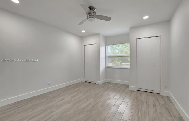 unfurnished bedroom with light wood-type flooring, ceiling fan, and multiple closets