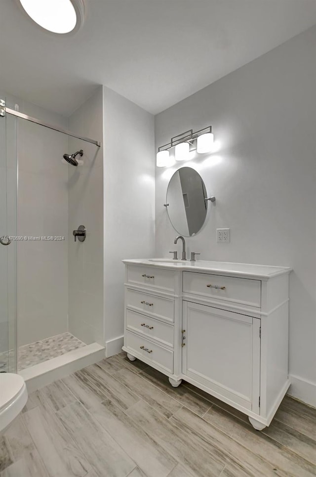 bathroom featuring a tile shower, hardwood / wood-style floors, vanity, and toilet