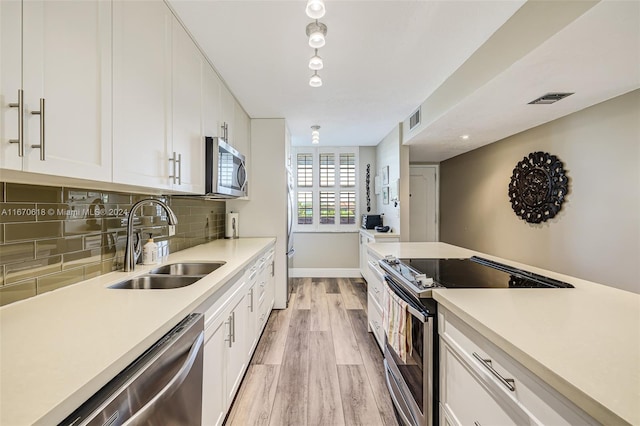 kitchen with white cabinets, sink, appliances with stainless steel finishes, light hardwood / wood-style floors, and decorative backsplash