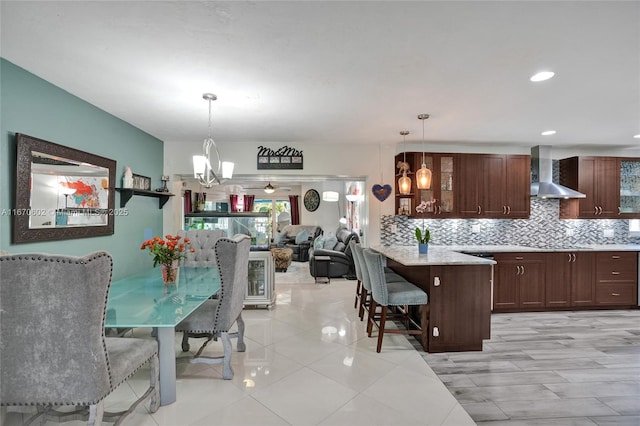 kitchen featuring a breakfast bar, a chandelier, decorative backsplash, hanging light fixtures, and wall chimney range hood