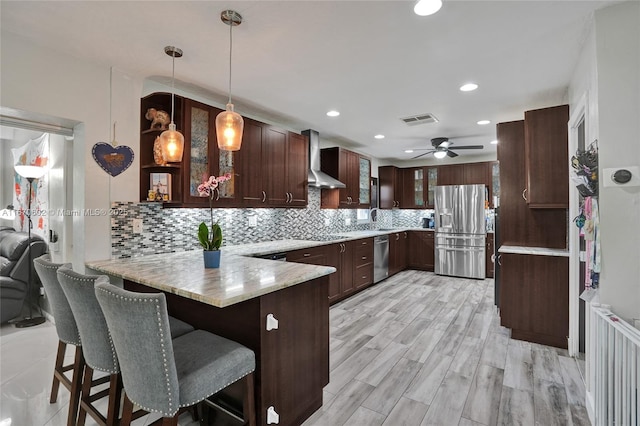 kitchen with appliances with stainless steel finishes, a breakfast bar, hanging light fixtures, kitchen peninsula, and wall chimney exhaust hood