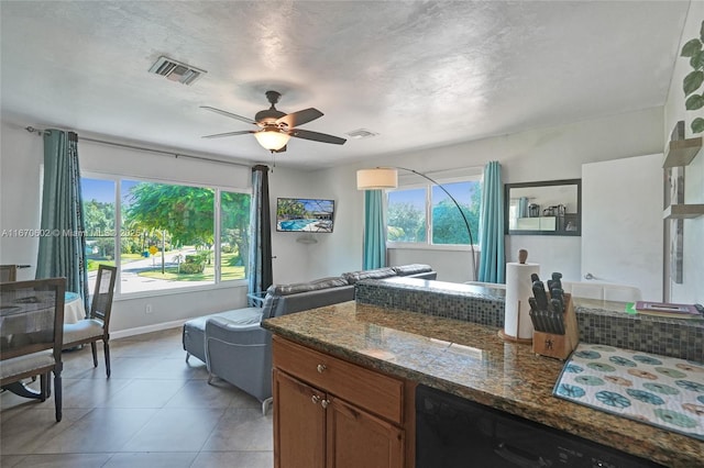 kitchen with light tile patterned flooring, a textured ceiling, black dishwasher, ceiling fan, and dark stone counters