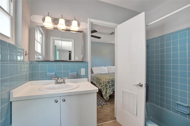 bathroom with vanity, tile patterned flooring, ceiling fan, tiled shower / bath combo, and tile walls