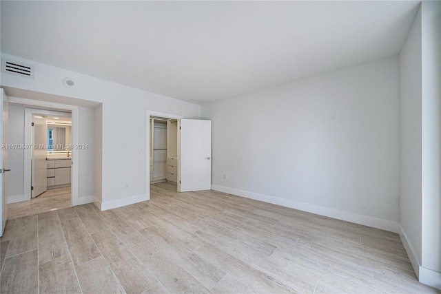 unfurnished bedroom featuring a walk in closet, ensuite bathroom, a closet, and light hardwood / wood-style floors