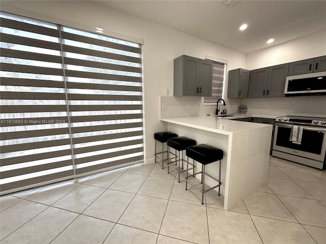 kitchen with appliances with stainless steel finishes, kitchen peninsula, light tile patterned floors, gray cabinets, and a kitchen bar