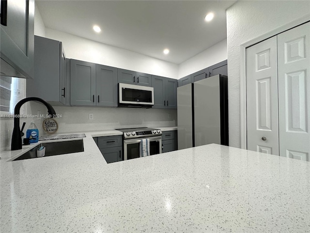 kitchen with gray cabinets, stainless steel appliances, light stone countertops, and sink