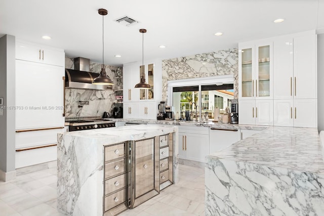 kitchen featuring wall chimney range hood, light stone counters, white cabinetry, stainless steel appliances, and a center island