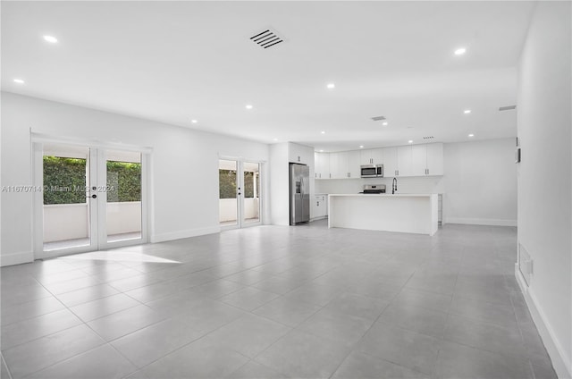 unfurnished living room featuring light tile patterned floors, sink, and french doors