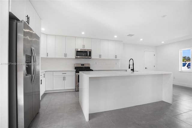 kitchen with appliances with stainless steel finishes, tasteful backsplash, light tile patterned floors, a center island with sink, and white cabinets