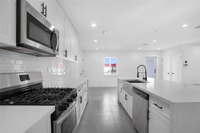 kitchen featuring backsplash, a kitchen island with sink, tile patterned flooring, white cabinetry, and stainless steel appliances