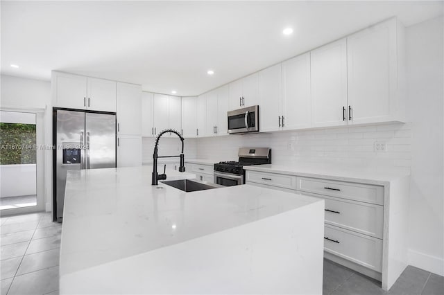 kitchen with a center island with sink, sink, tile patterned flooring, appliances with stainless steel finishes, and white cabinetry