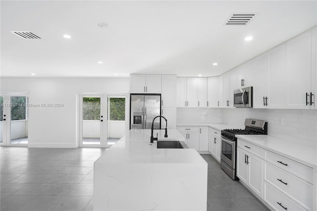 kitchen featuring appliances with stainless steel finishes, french doors, sink, white cabinets, and an island with sink