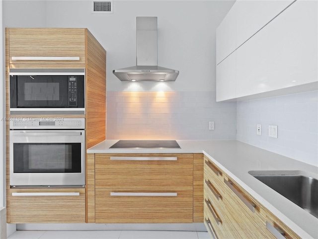 kitchen featuring black electric stovetop, oven, decorative backsplash, built in microwave, and range hood