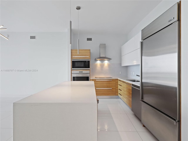 kitchen featuring pendant lighting, wall chimney range hood, built in appliances, decorative backsplash, and white cabinetry