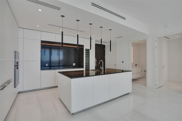 kitchen with hanging light fixtures, a center island with sink, white cabinetry, and sink